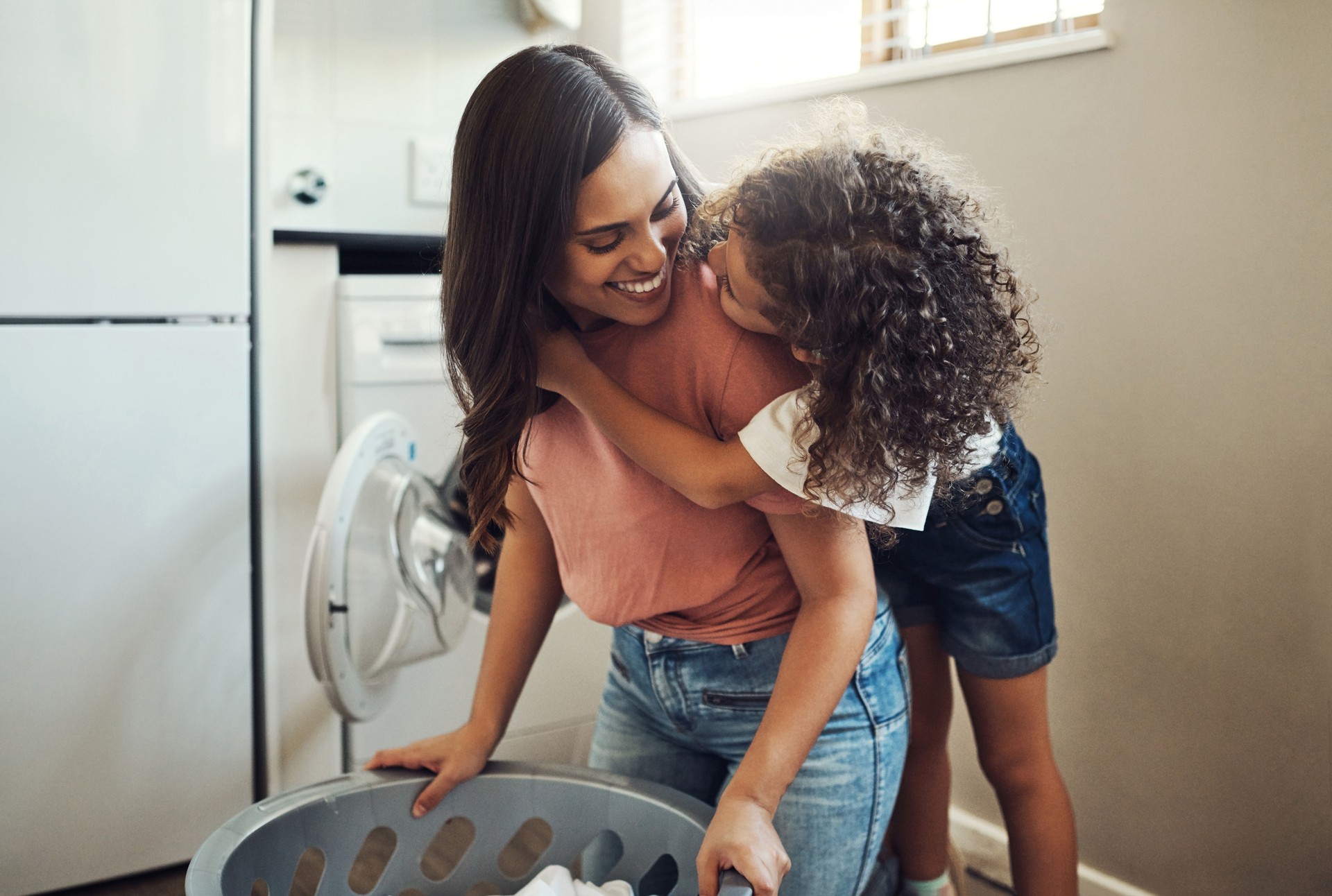Shot of an adorable young girl hugging her mother while helping her with the laundry at home